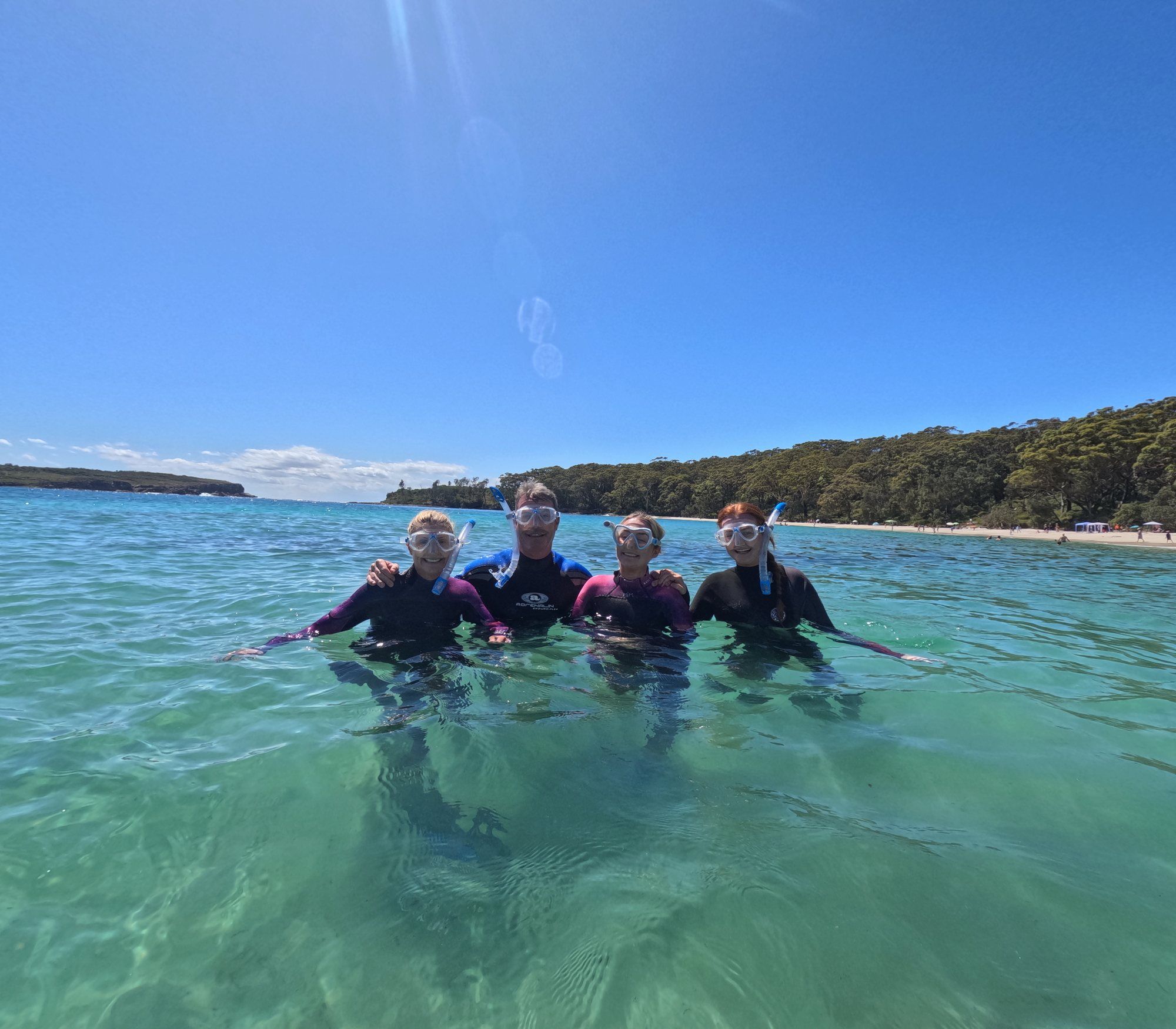 Four smiling students in masks standing in clear, shallow turquoise water in Jervis Bay